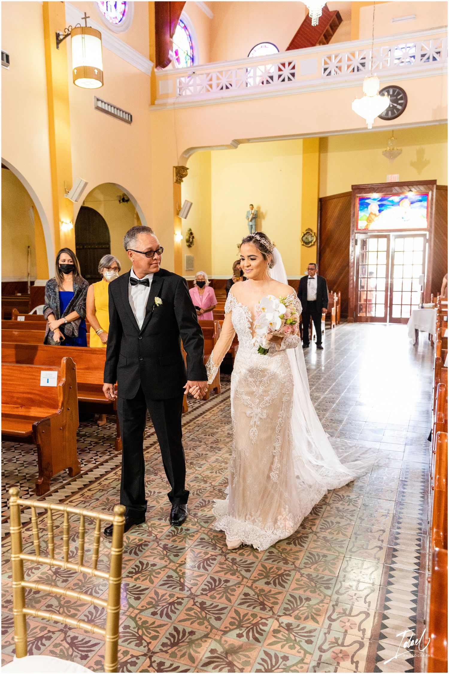 A wedding ceremony processional in a beautiful yellow-walled Catholic church with ornate details.