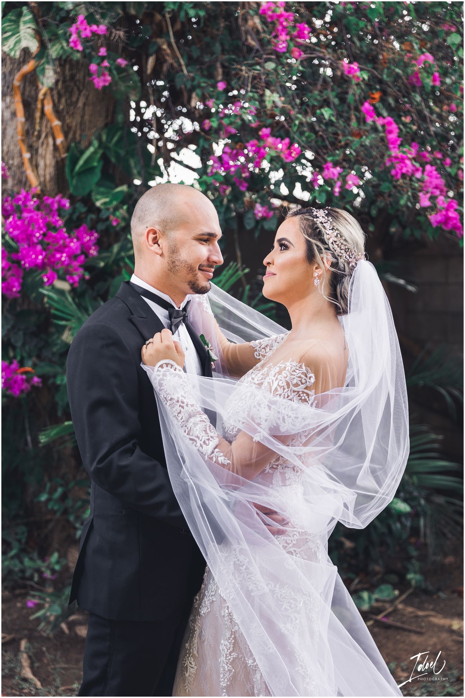A loving wedding couple shares a tender moment surrounded by bright pink bougainvillea flowers.
