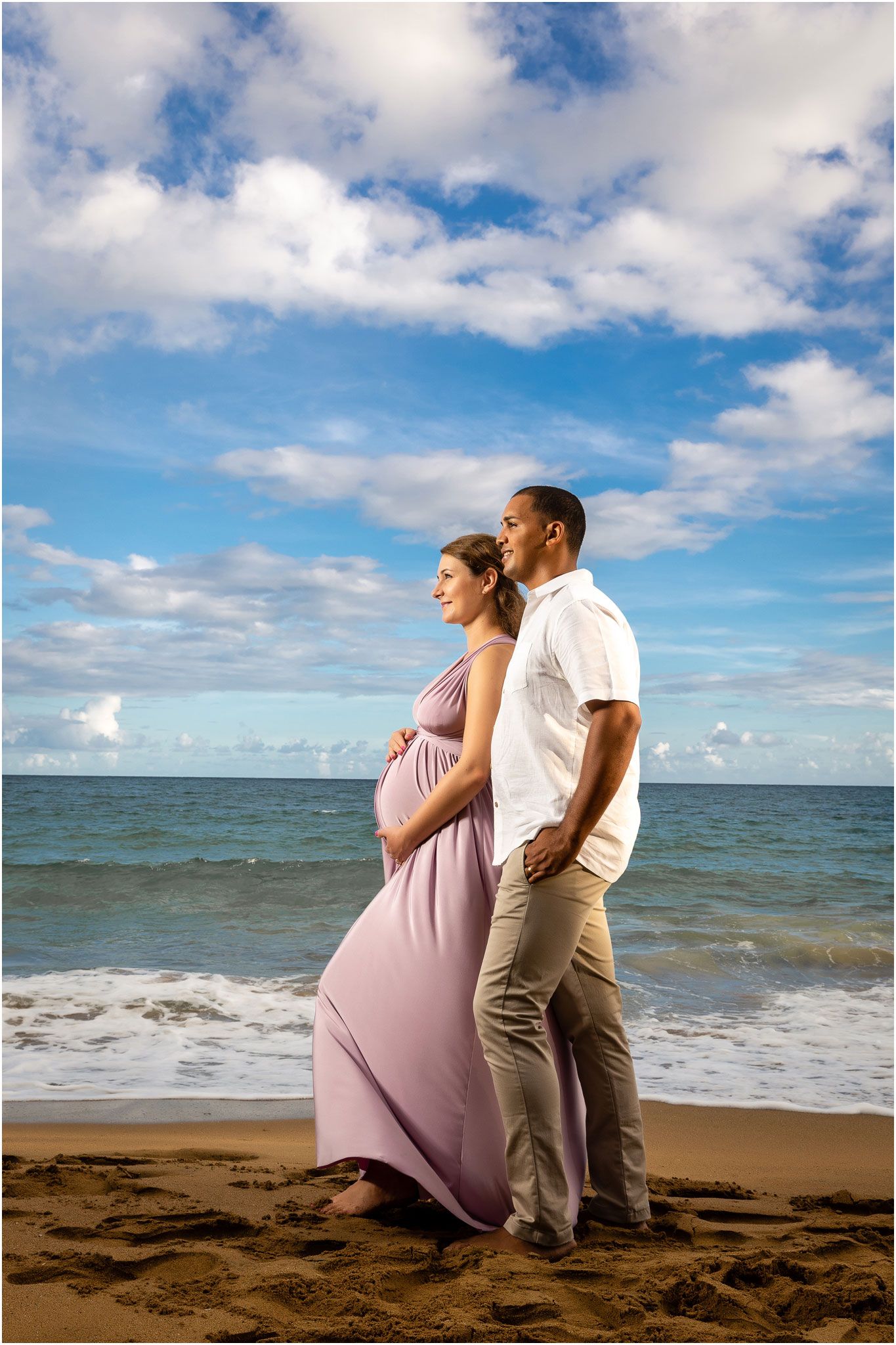 Couple poses together against ocean backdrop during sunset beach maternity session.