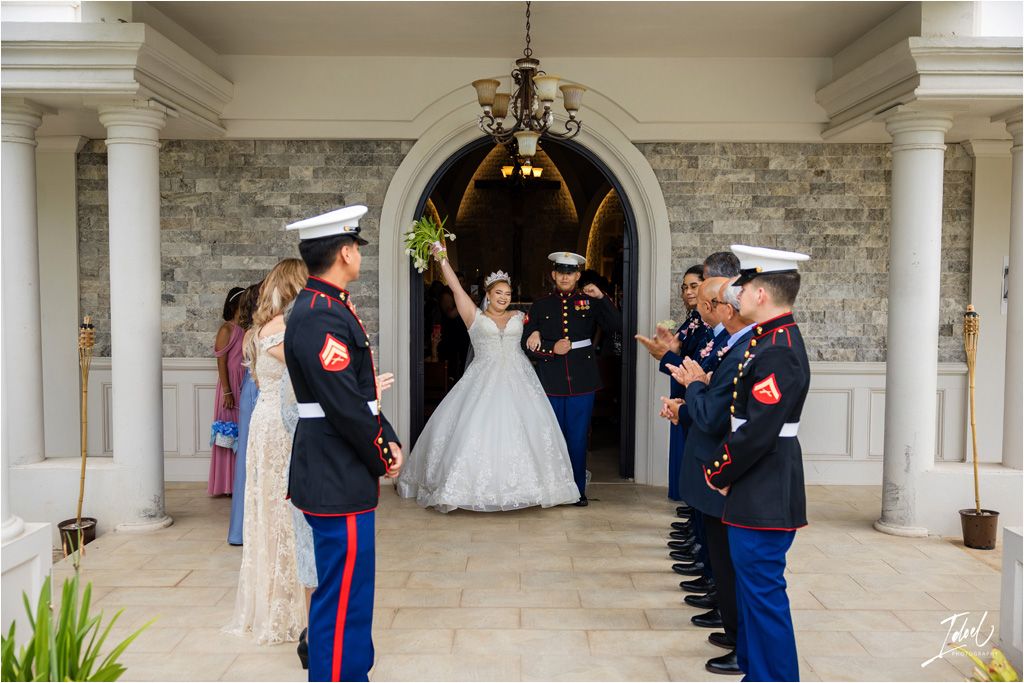 Military service members in dress uniforms form an honor guard outside a stone church entrance during a wedding.