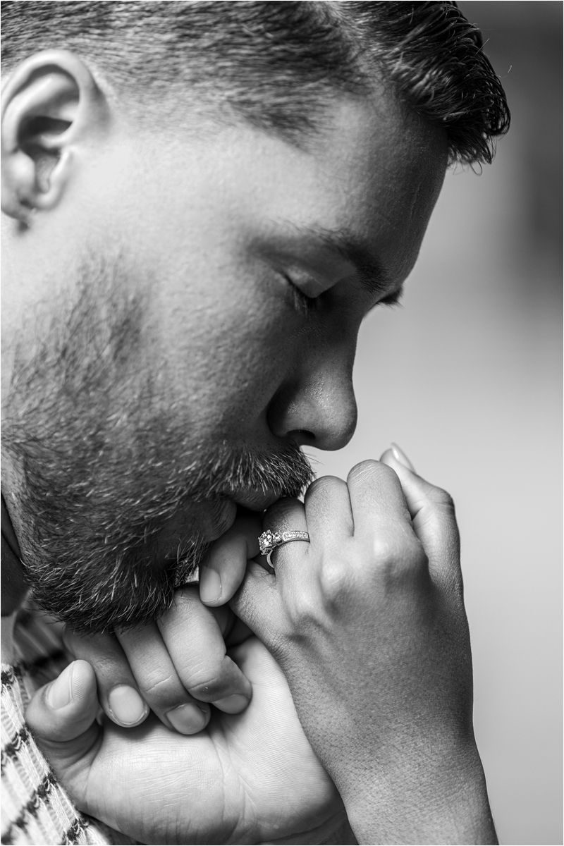 A close-up monochrome portrait showing hands clasped in prayer with a ring on one finger, captured in a reflective pose.