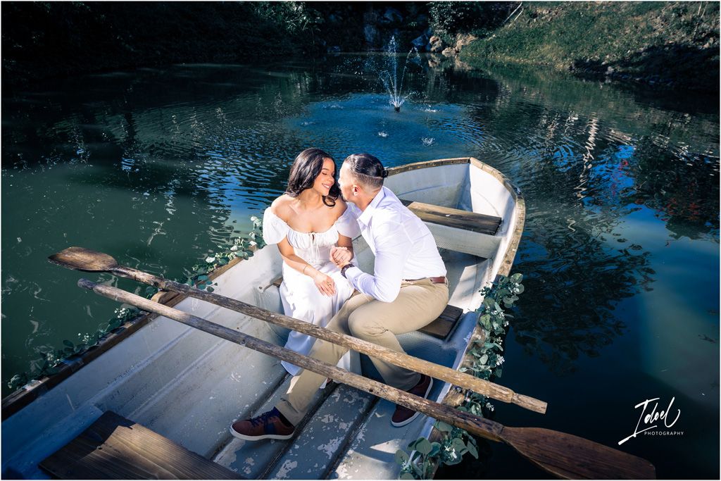 Intimate moment captured of a couple in white clothing embracing in a wooden boat on reflective blue waters.
