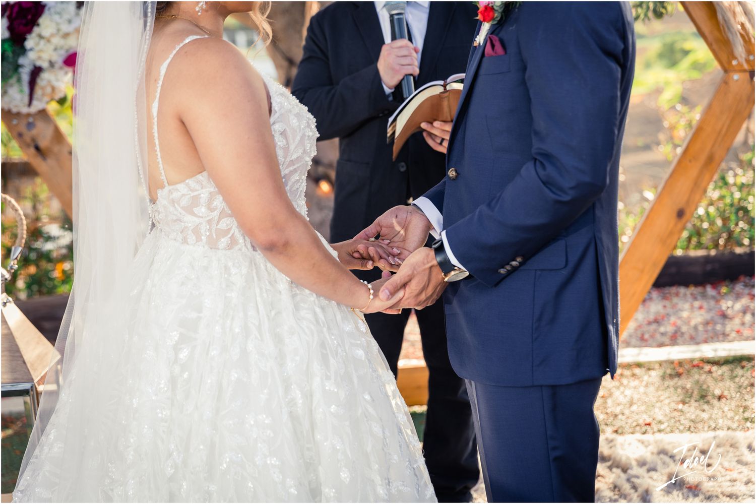 Close-up of couple holding hands during wedding ceremony with lace dress details.