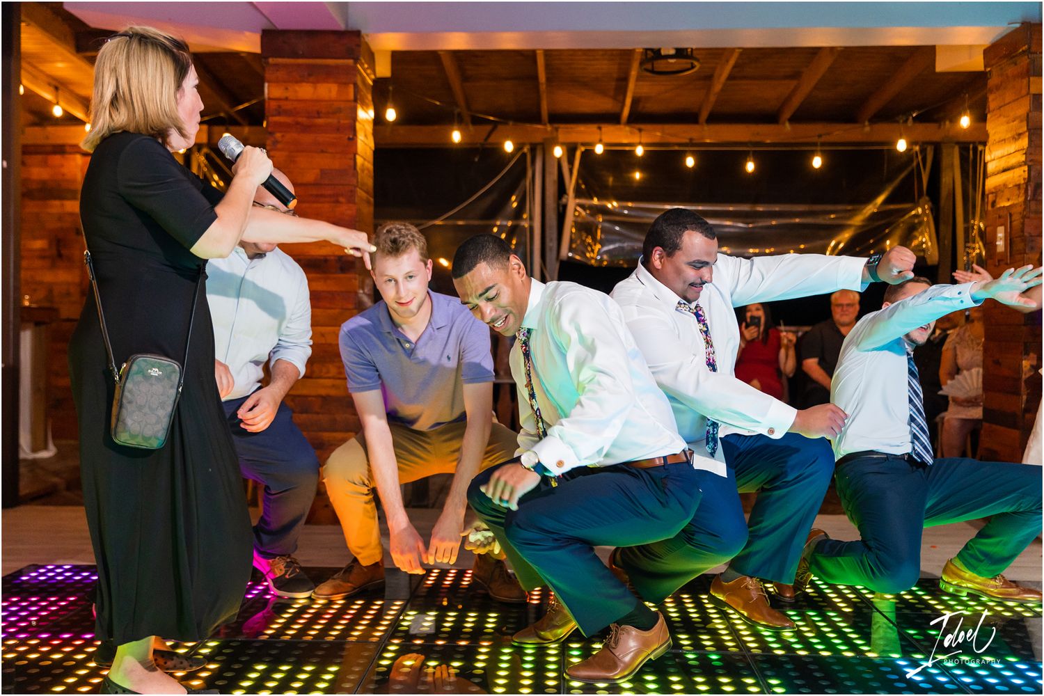 Wedding guests performing energetic dance moves on a colorful light-up floor at a reception.