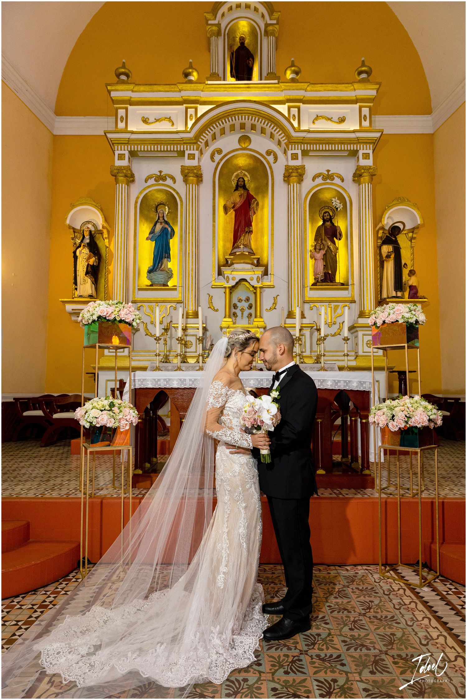 Newlyweds share an intimate moment in a ornate church with a golden altar and religious statues.
