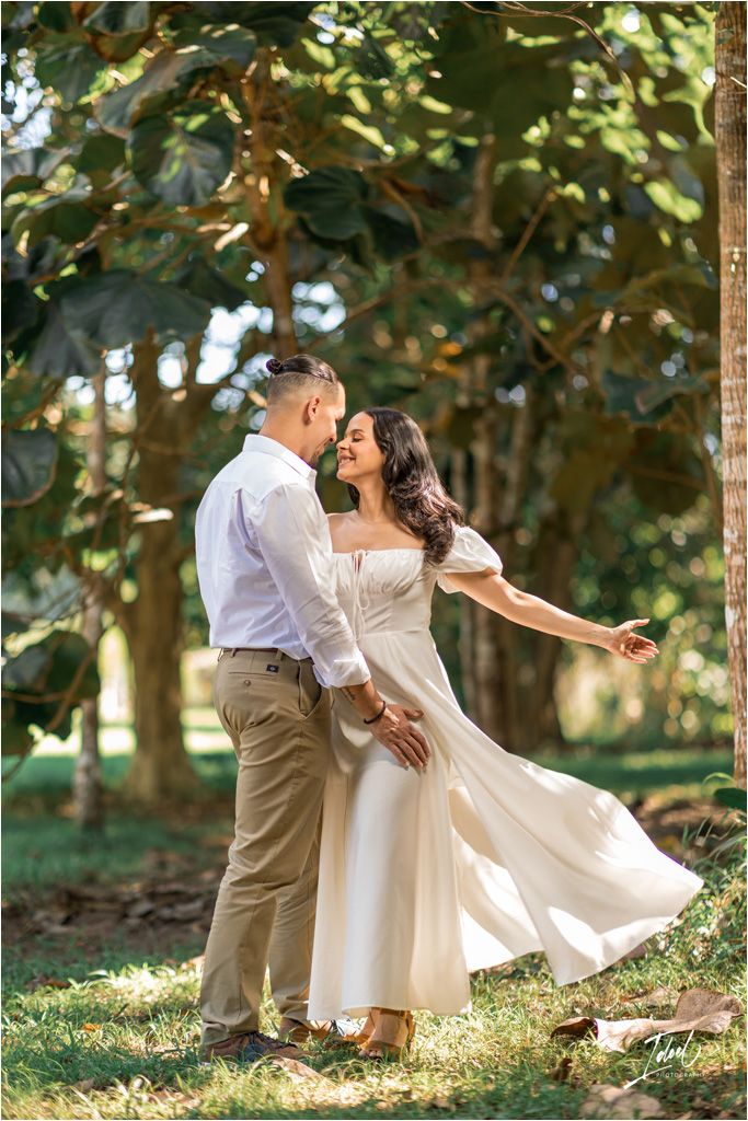 A couple shares a romantic moment dancing outdoors in a garden setting with sunlight filtering through the trees.