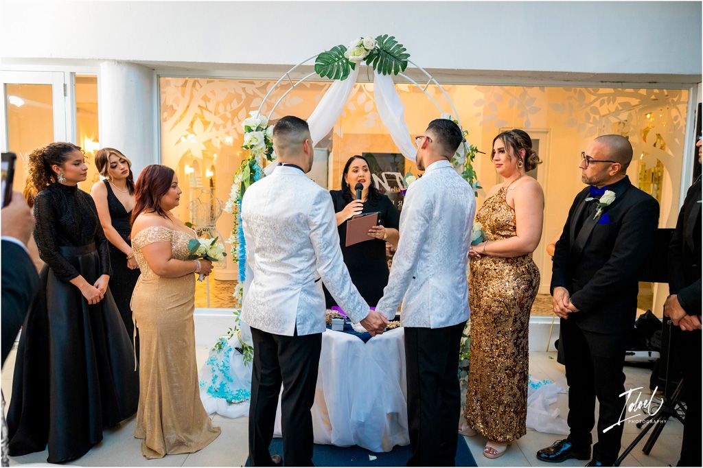 A wedding ceremony takes place in a bright indoor venue with a decorative wall mural and people gathered in formal attire.