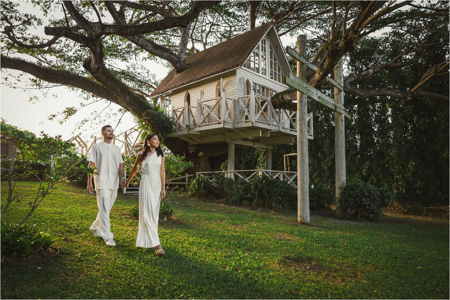 Wedding couple walking along a rustic wooden veranda surrounded by greenery.