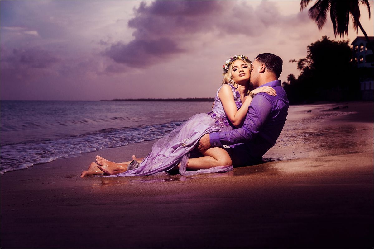 Romantic couple embraces on a tropical beach at sunset with dramatic purple sky and ocean waves.