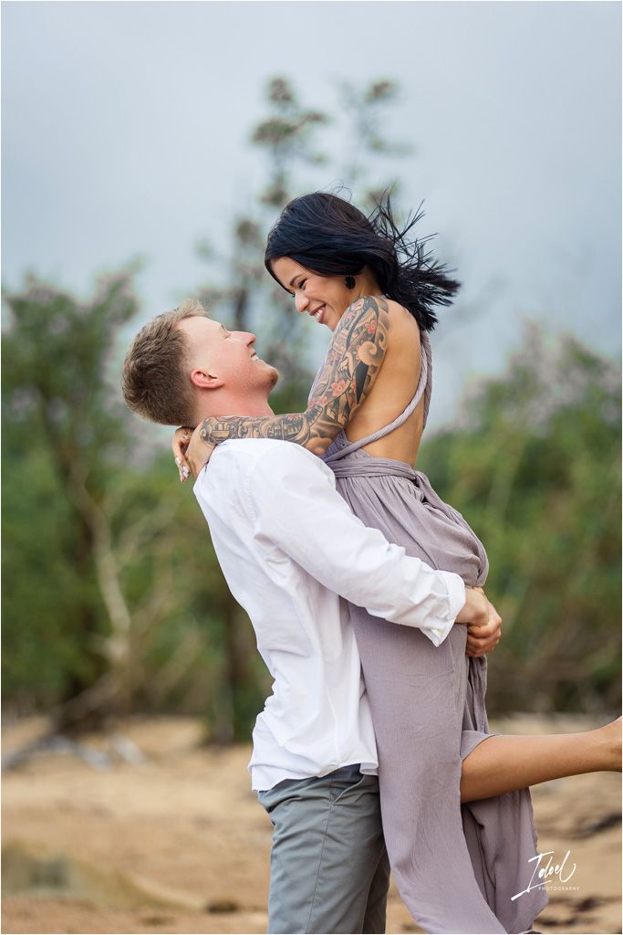 Romantic couple embracing outdoors with visible tattoos and flowing dress.