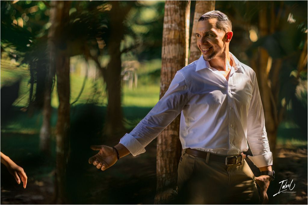Someone in a white dress shirt and dark pants stands in warm sunlight among trees in a wooded outdoor setting.