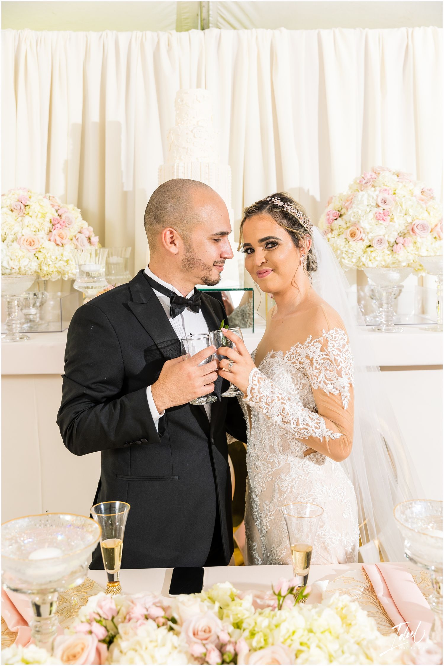 A romantic champagne toast moment between newlyweds at their flower-decorated reception table.