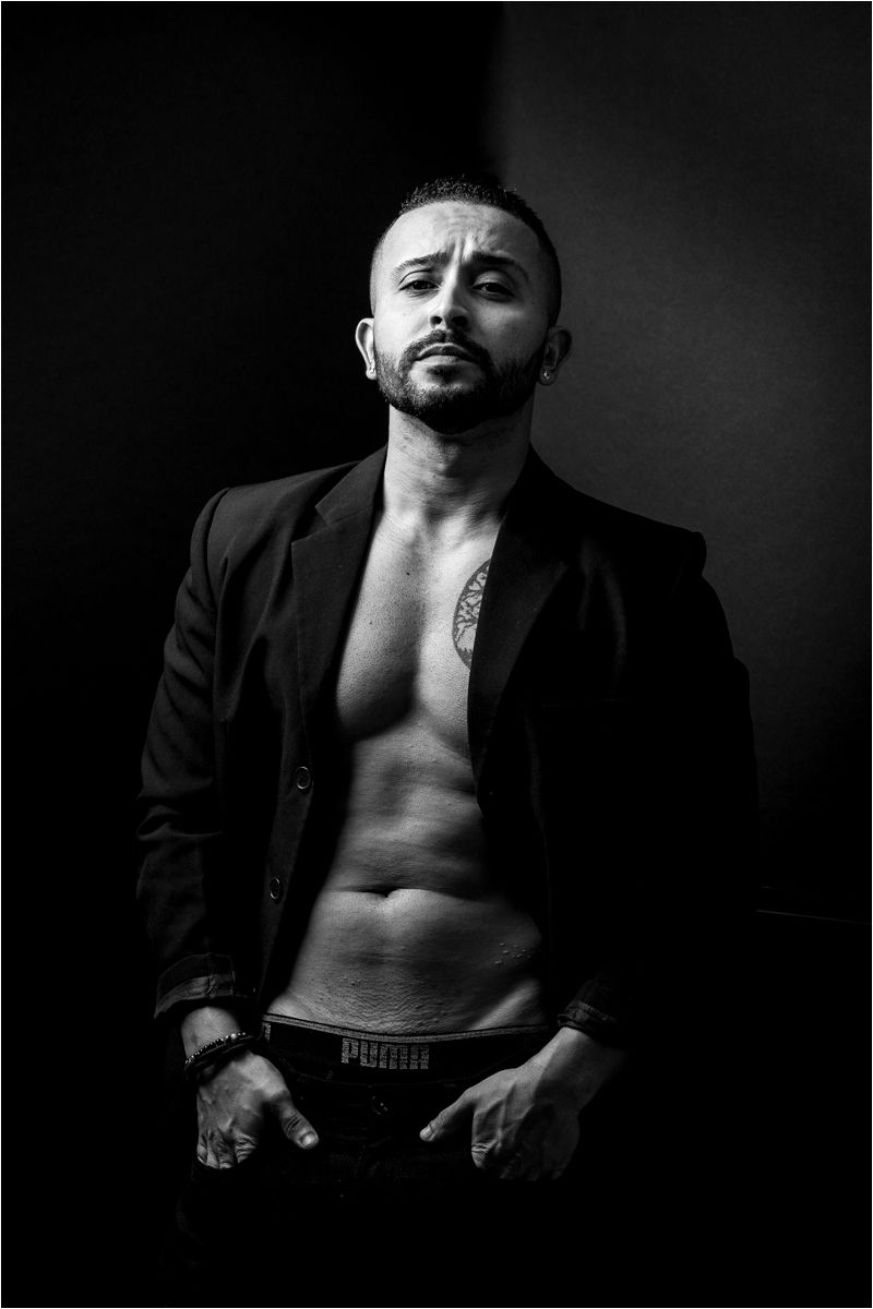 Artistic black and white portrait series showing shirtless man in dramatic lighting wearing dark blazer against dark background.