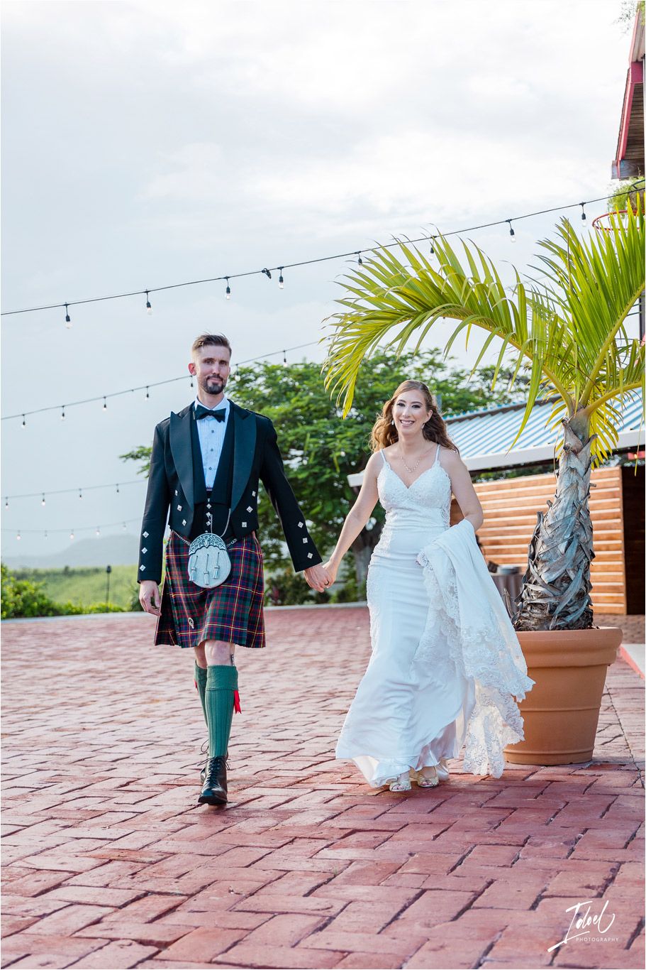 A couple walks hand in hand on brick pavement, combining Scottish tradition with modern wedding style.