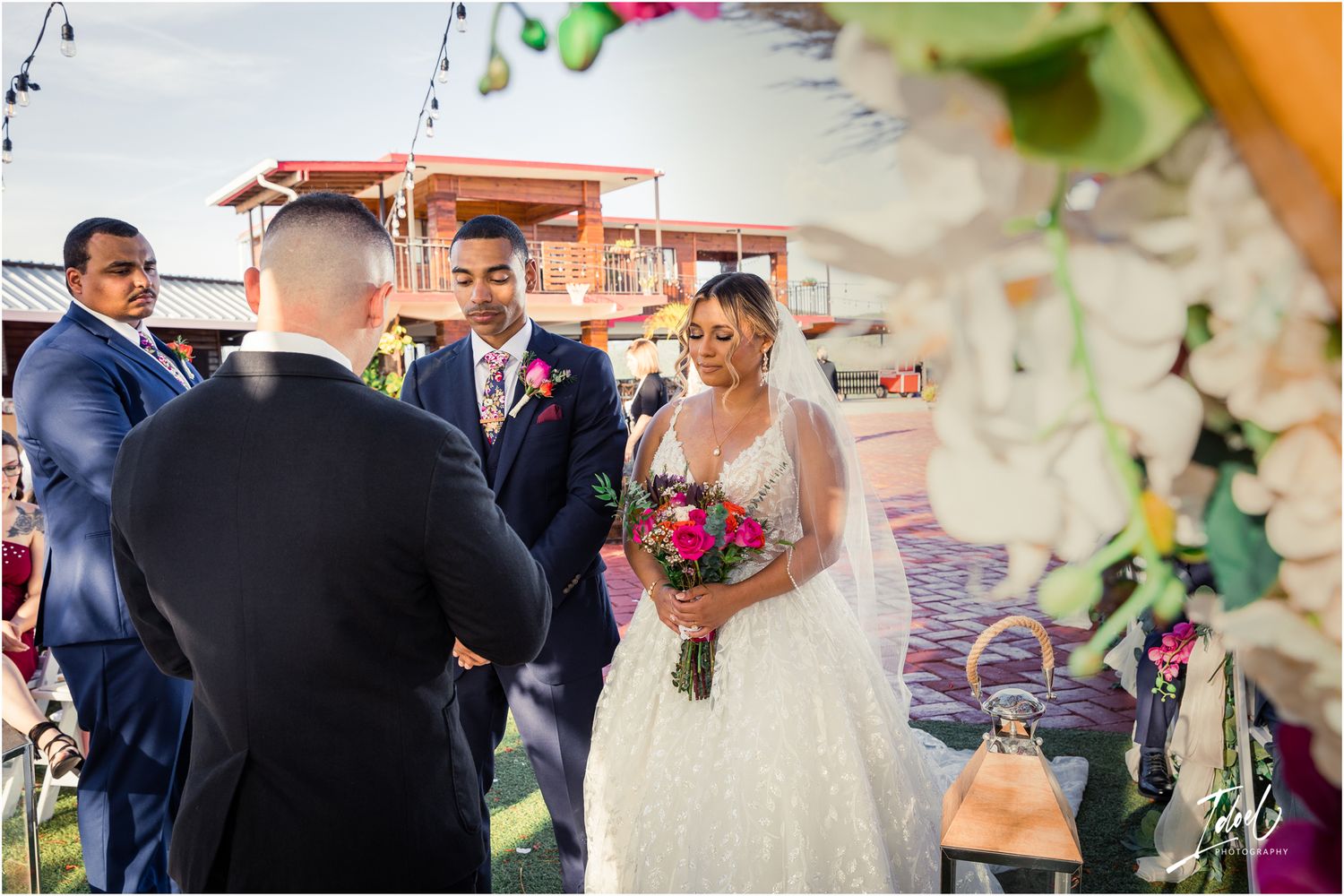 Wedding ceremony with colorful floral arrangements and a terra cotta building backdrop.