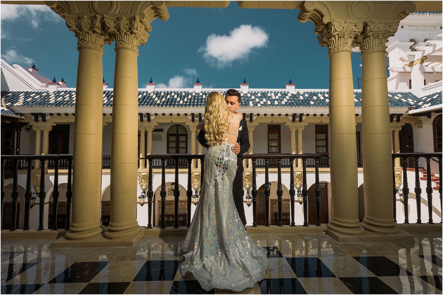 A silver sequined gown with a flowing train photographed in an elegant columned gallery with checkered floors.
