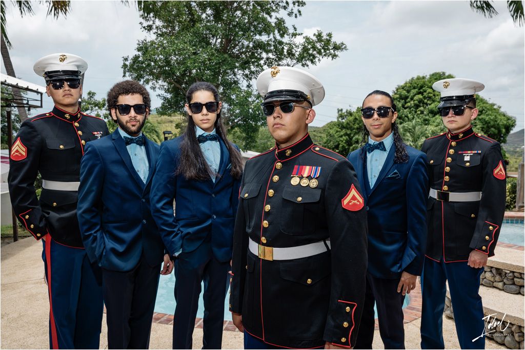 Military service members pose with groomsmen in blue suits at an outdoor wedding.