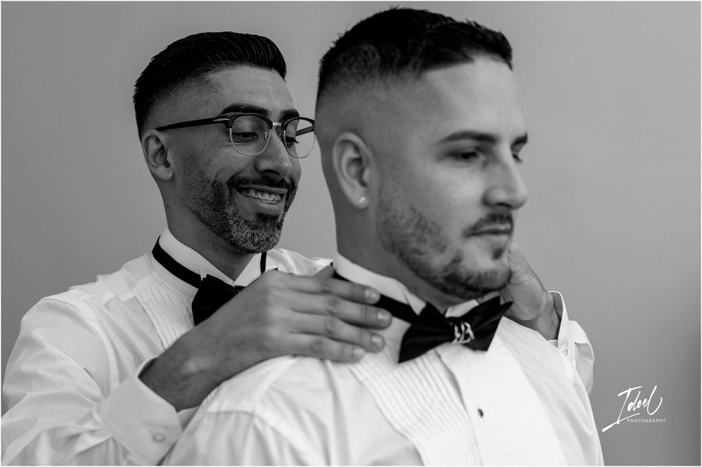 A black and white photo of a groom having his bowtie adjusted by his best man before the ceremony.