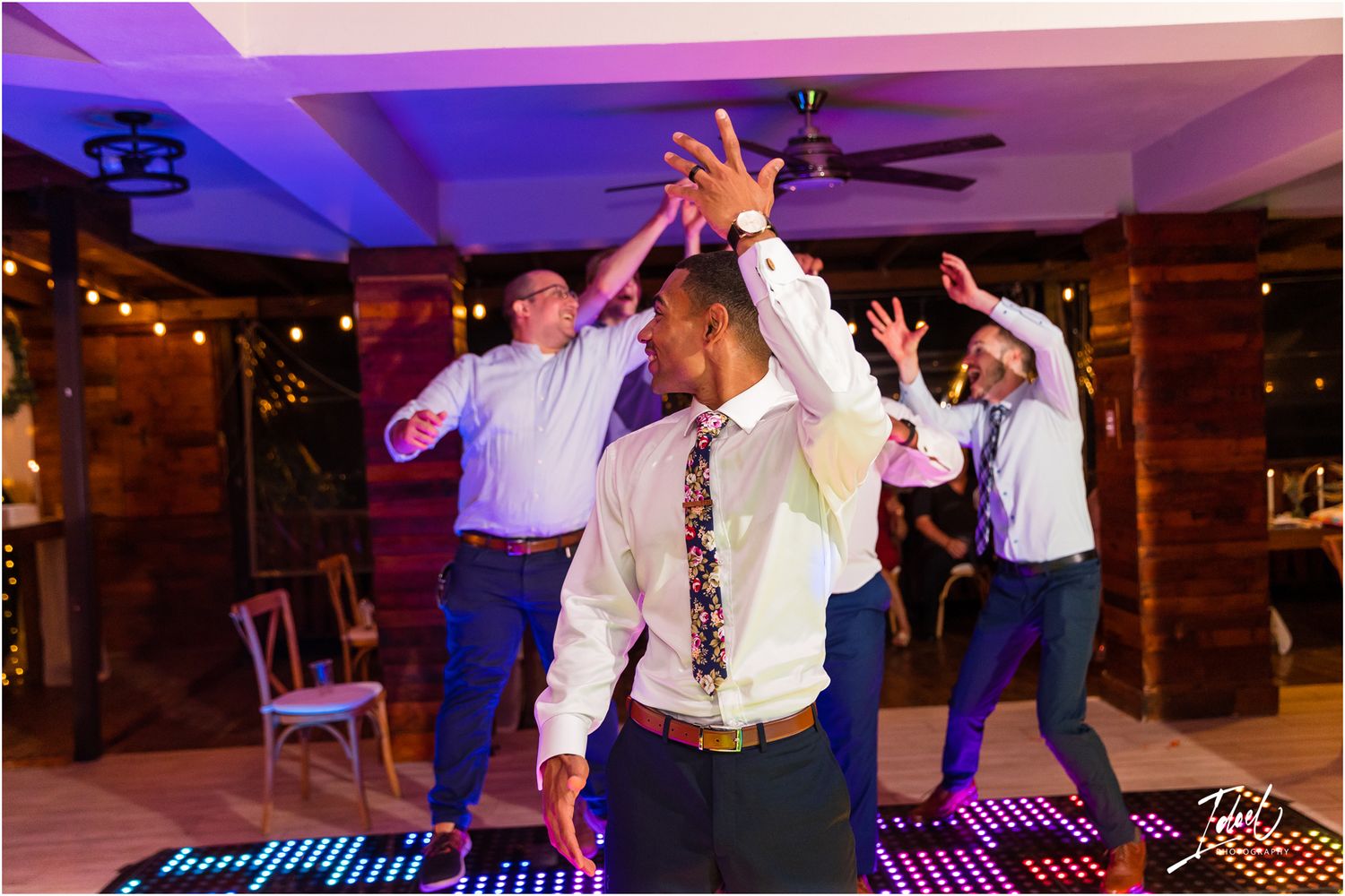 Party guests dancing enthusiastically on a purple-lit dance floor at an indoor venue.