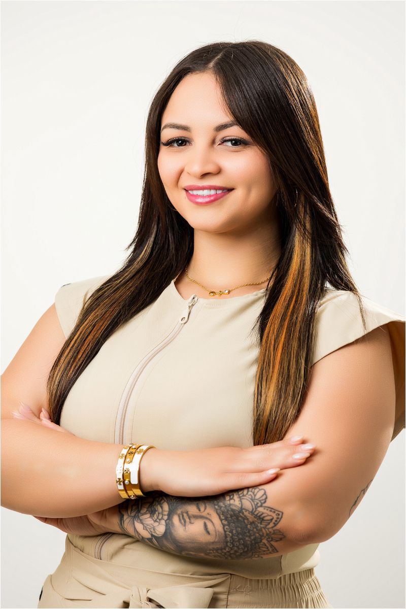 A woman in a beige sleeveless top poses playfully in a series of studio portraits showing off an arm tattoo.