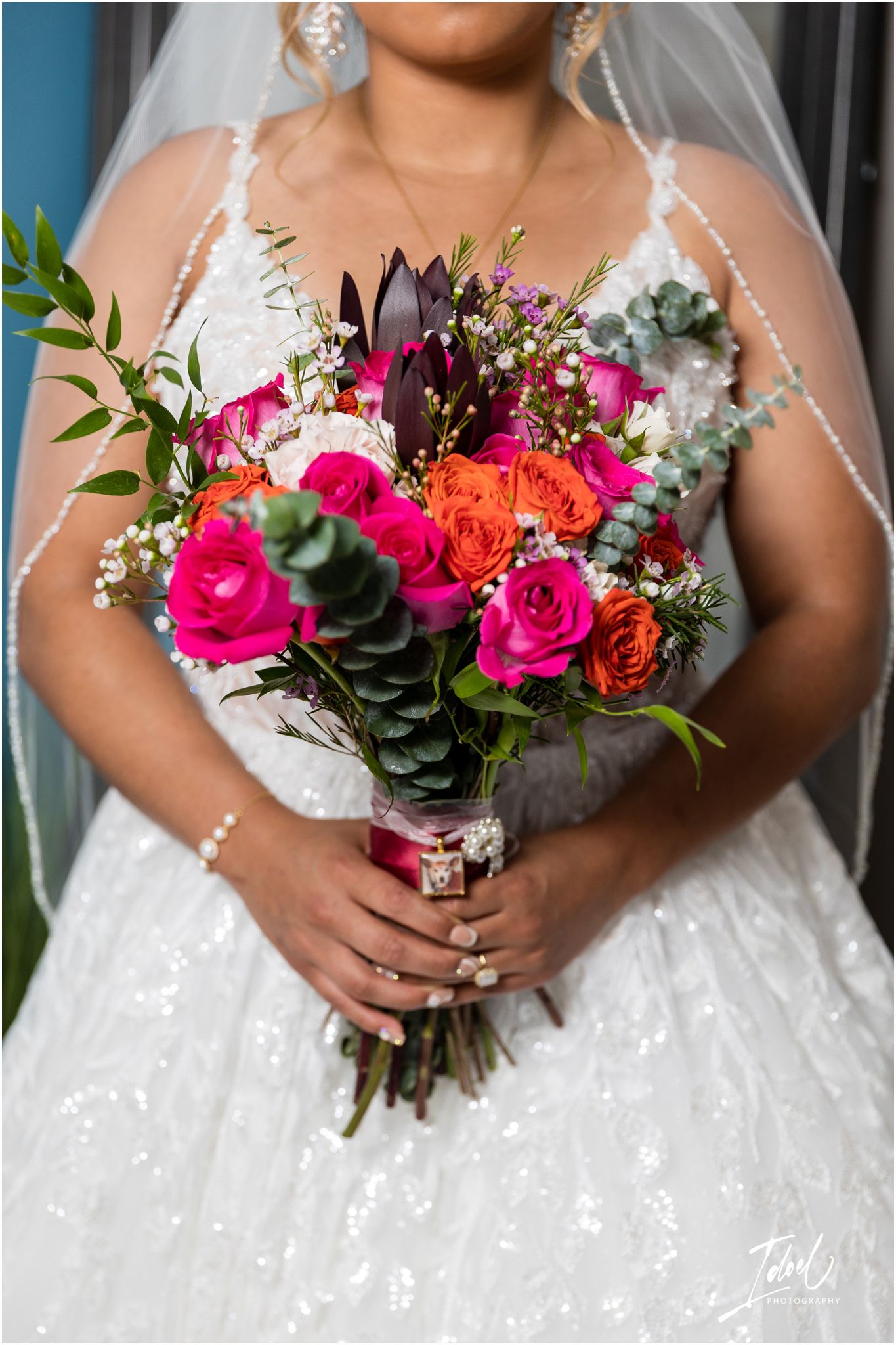 Close-up of colorful bridal bouquet with pink roses and purple flowers against white wedding dress.