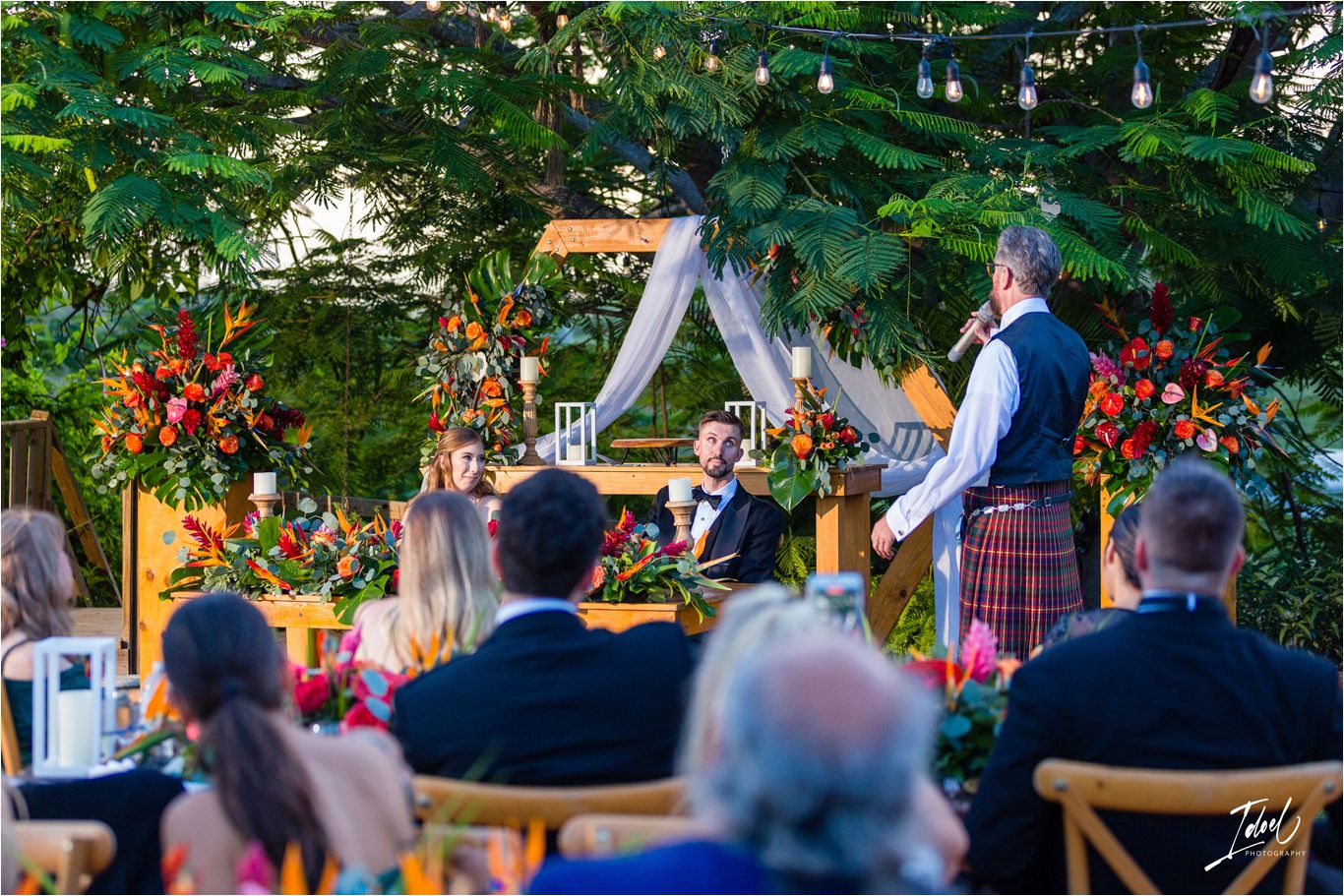 Outdoor wedding ceremony setup with white draping and vibrant orange floral arrangements.
