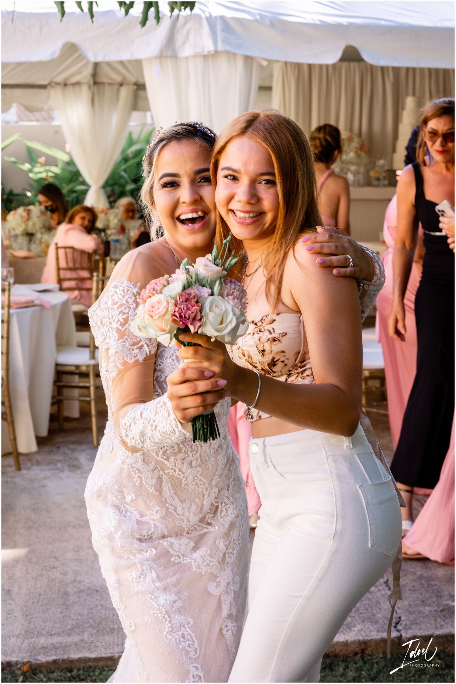 Two wedding attendees sharing a joyful moment while holding a small floral bouquet.