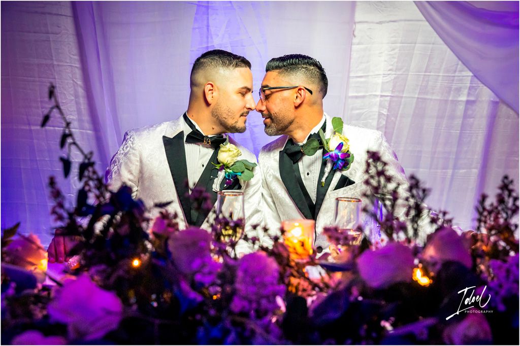 Wedding couple shares intimate moment during reception with purple lighting and floral decorations in foreground.