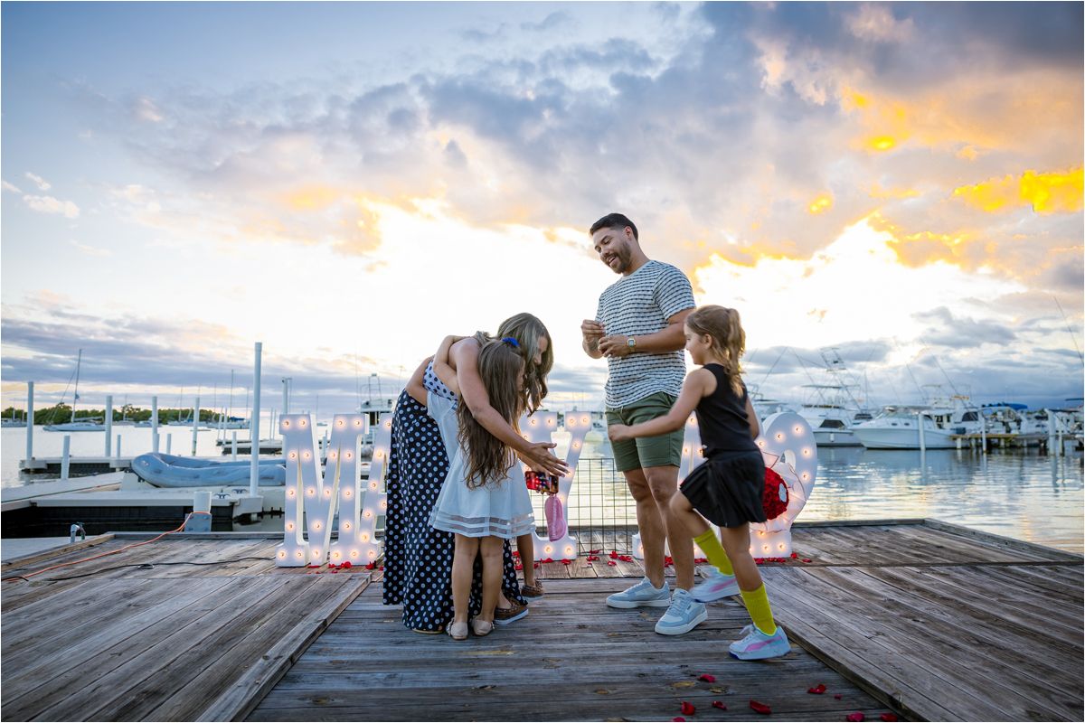 A family gathers together on a marina dock at sunset with boats and colorful sky in the background.