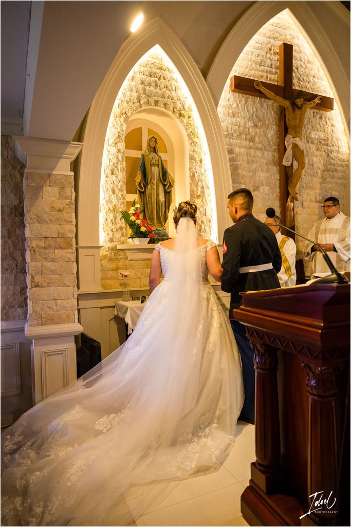 Wedding ceremony in a chapel with illuminated gothic arches and a long flowing white dress train.