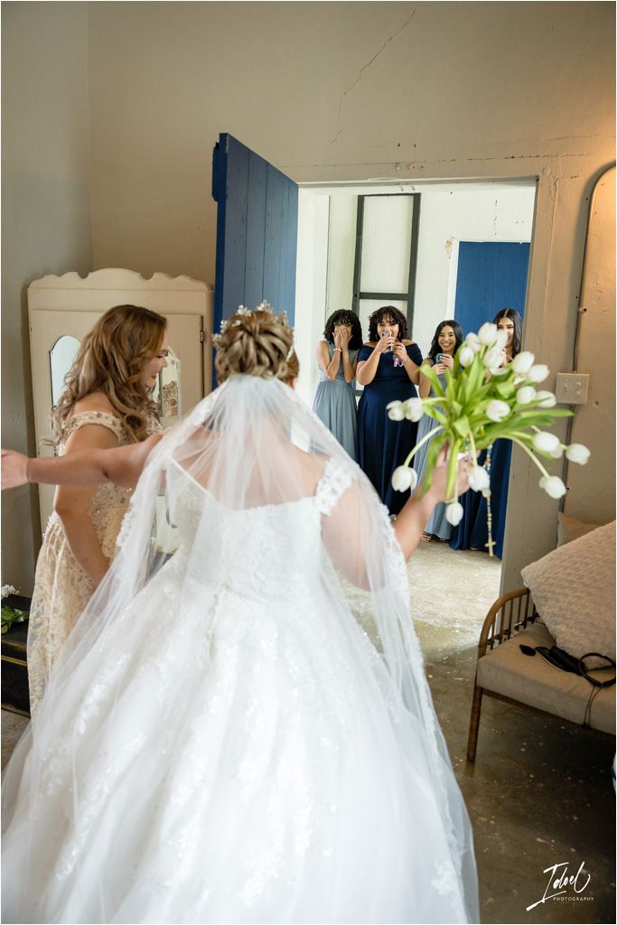 Wedding party members react with excitement as they see the bride in her gown.