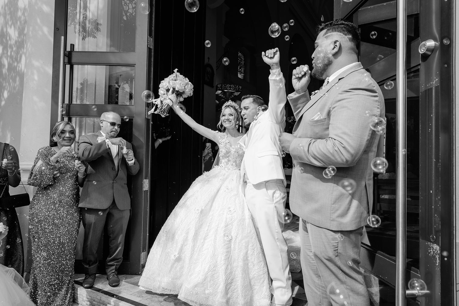 A black and white photograph shows a wedding celebration with people dancing and socializing at an indoor reception.