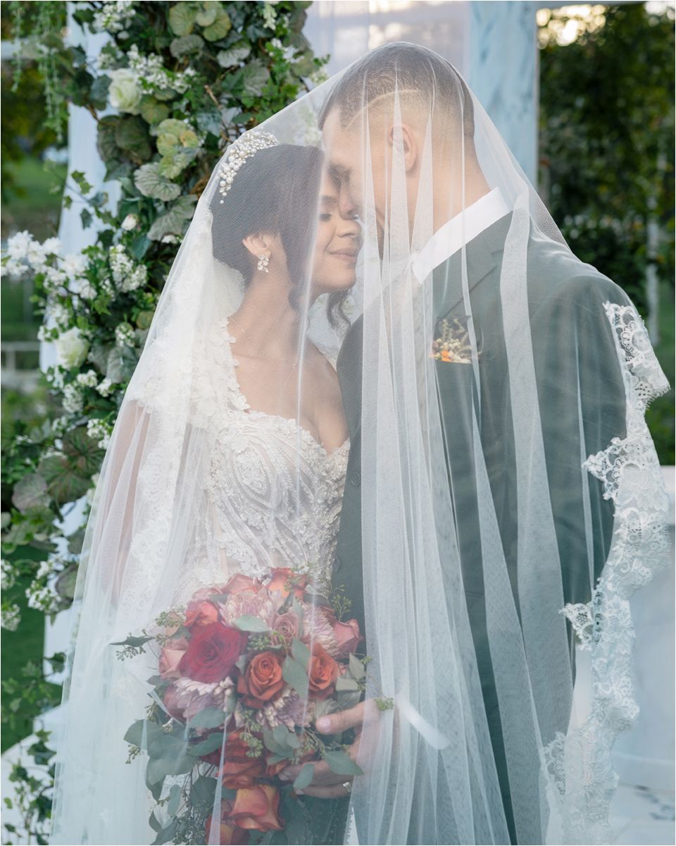 A romantic wedding scene through a delicate lace veil with floral arrangements in the background.