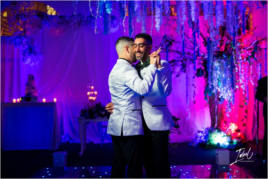 Two people share a romantic dance together under dramatic purple and blue lighting at an elegant event space.
