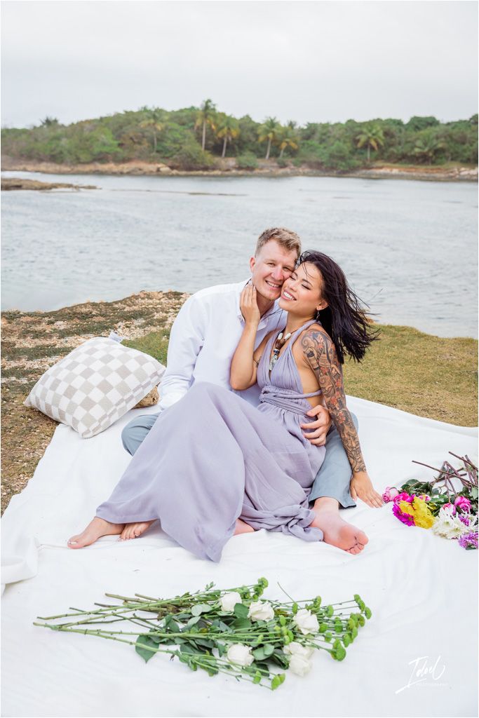 Romantic picnic scene on coastal cliff with flowers and white blanket.