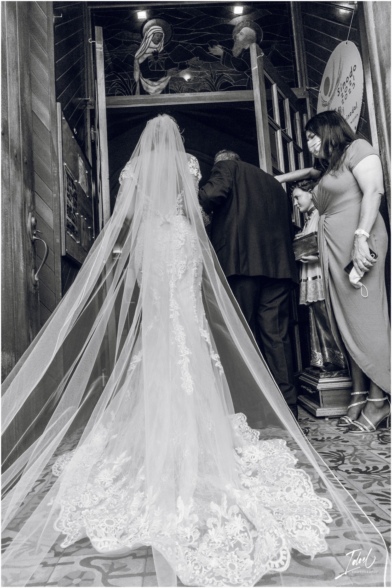 A dramatic black and white shot of a bride's detailed lace gown and cathedral veil from behind.