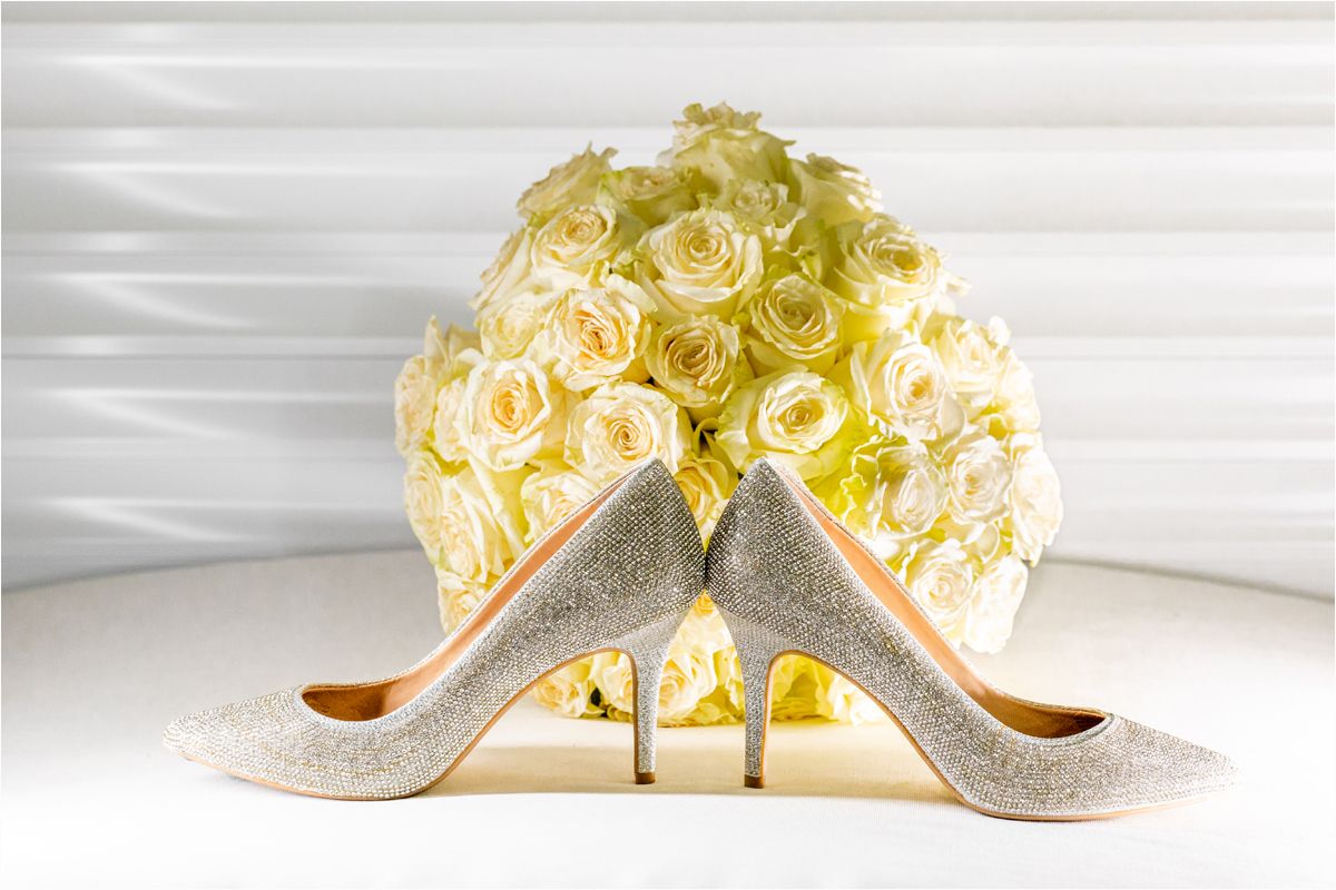 Elegant silver glitter wedding shoes displayed alongside yellow roses on a white surface.