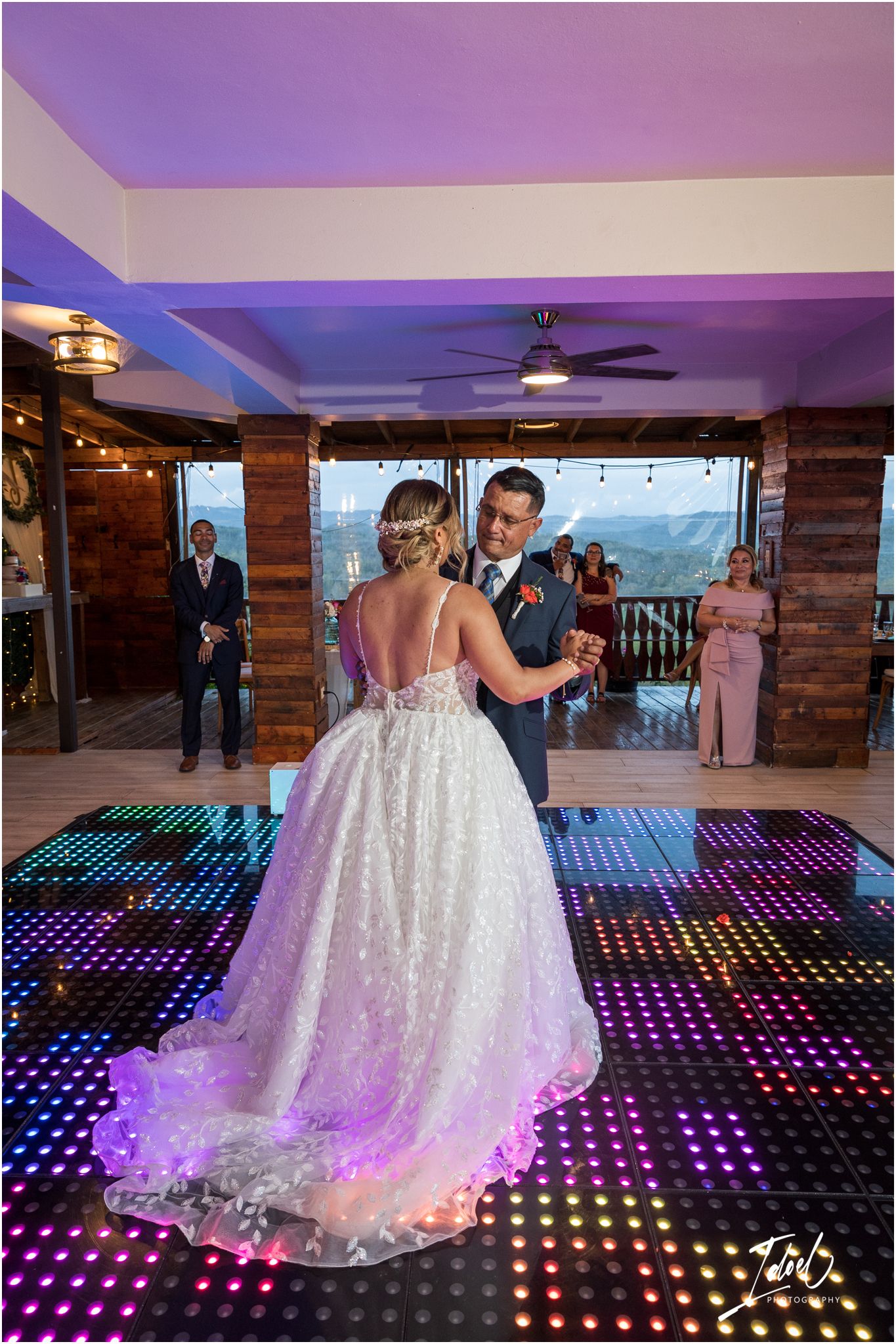 A couple shares their first dance on an illuminated LED dance floor with mountain views in the background.