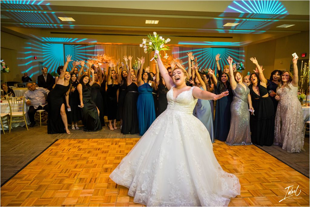 Wedding reception crowd cheering with raised hands as bride celebrates on dance floor.