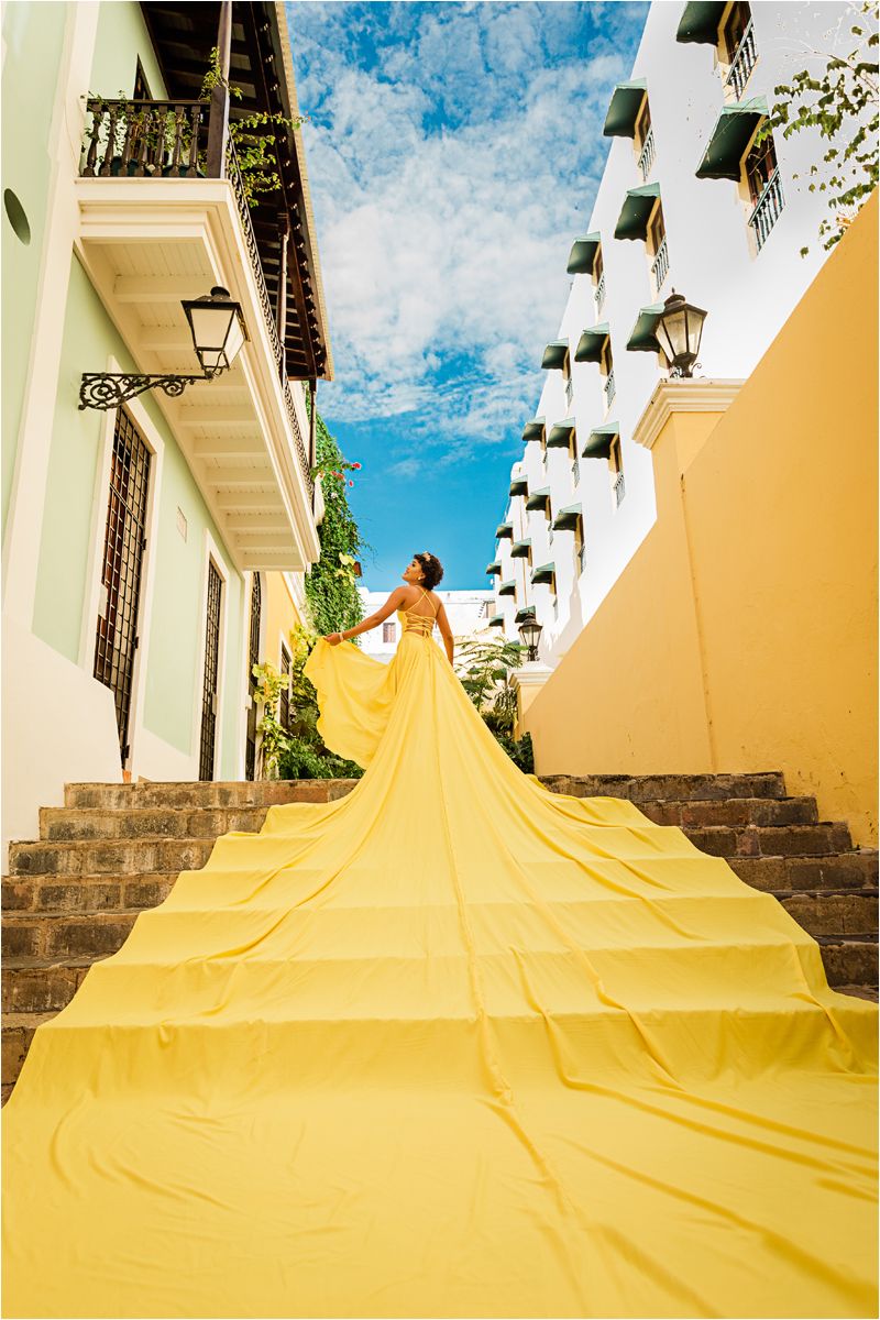 A bright yellow slip-n-slide extends down a series of steps at an outdoor venue against a blue sky.