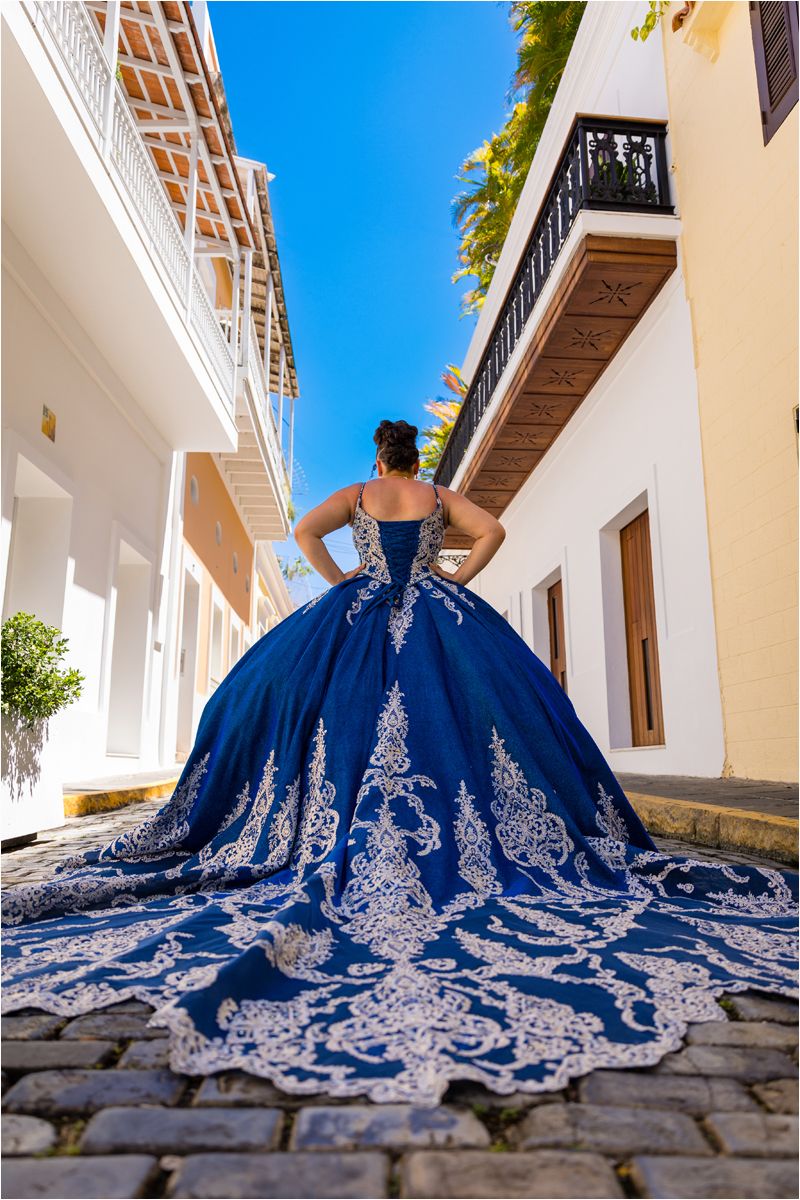 A stunning royal blue ball gown with intricate silver embroidery spreads across cobblestone pavement in a dramatic display.