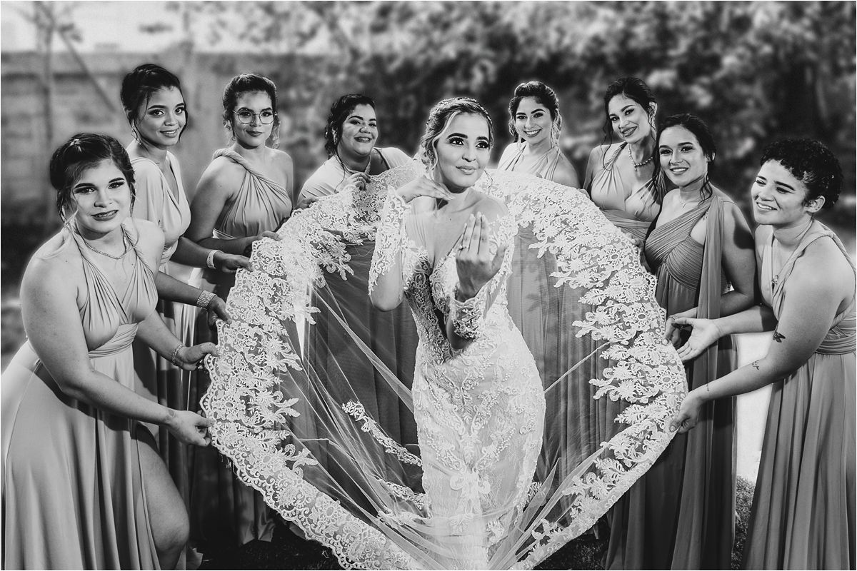 Bridesmaids in gray dresses help bride in lace gown prepare for wedding celebration.