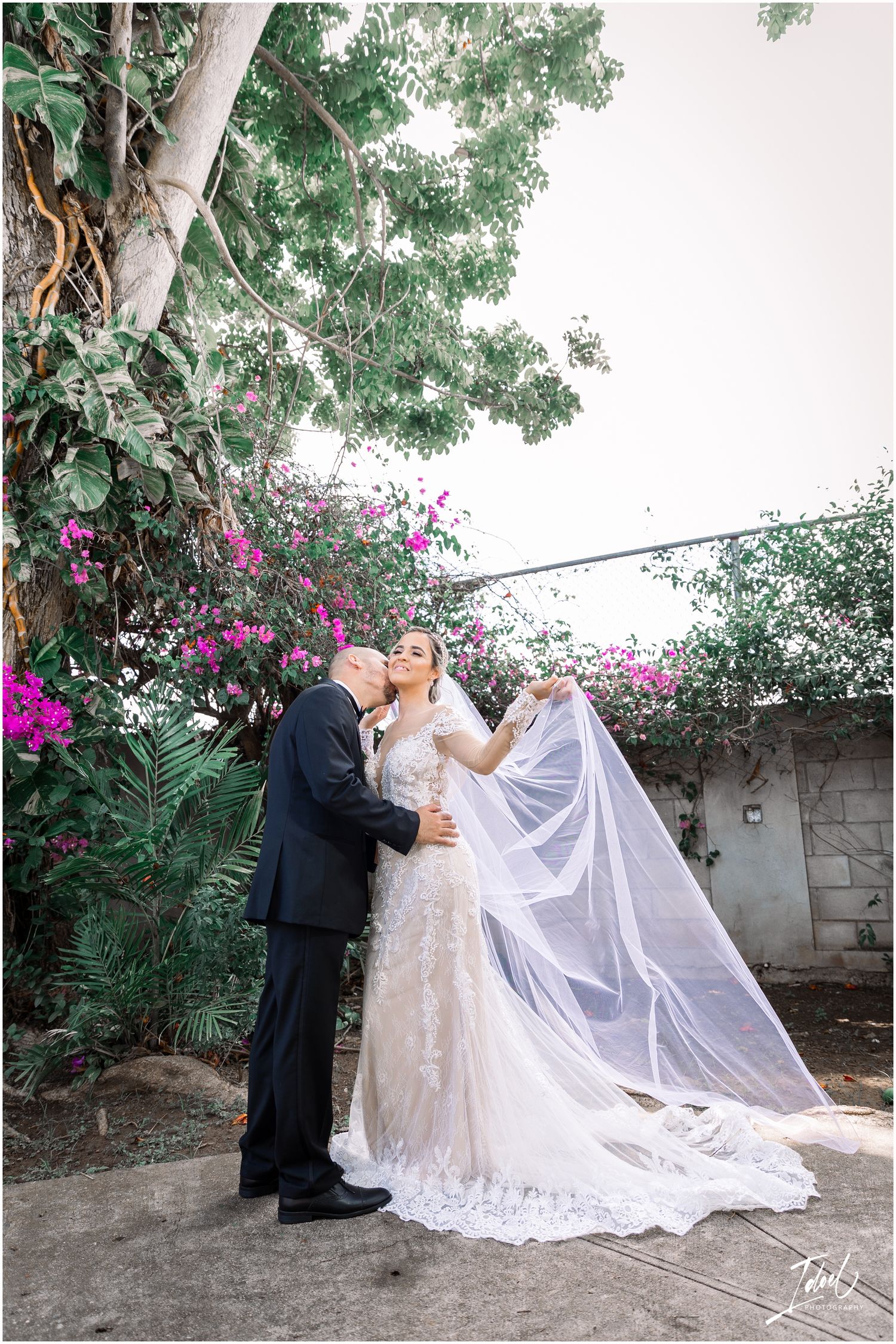 A wedding couple's tender moment captured against a backdrop of pink flowers and green foliage.
