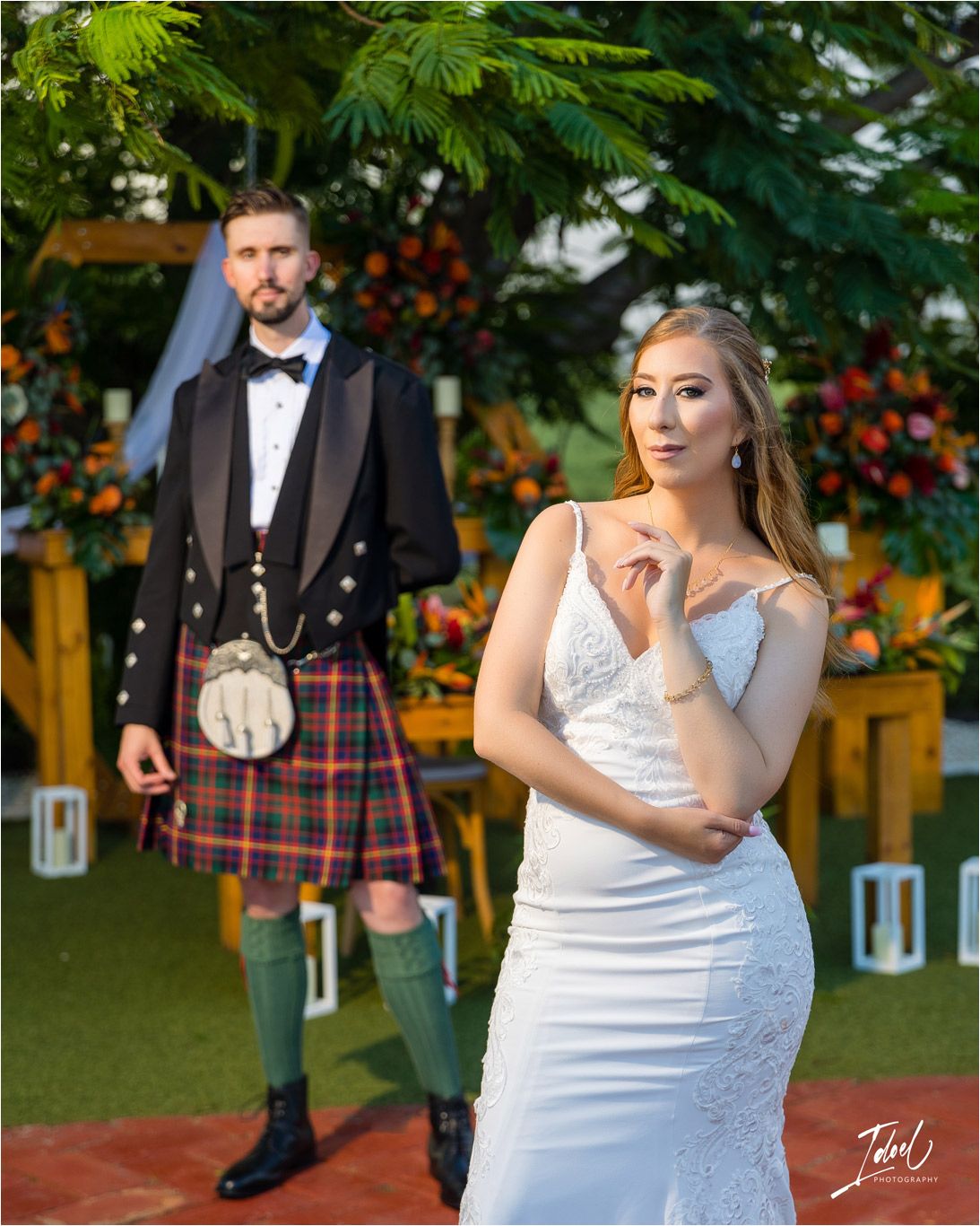 A couple in Scottish wedding attire poses separately against vibrant tropical garden decor.
