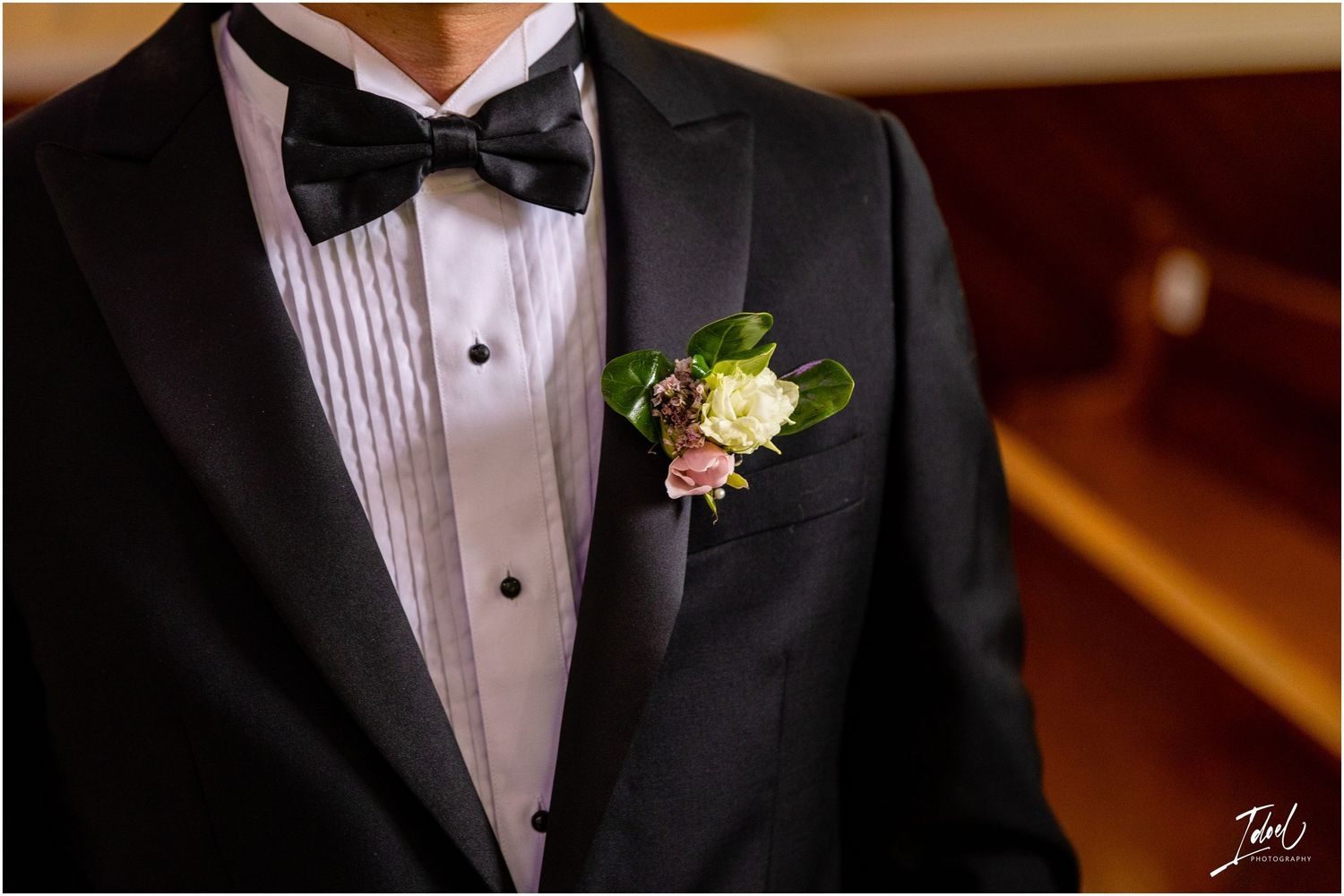 Close-up of groom's classic tuxedo with white boutonniere and pleated shirt detail.