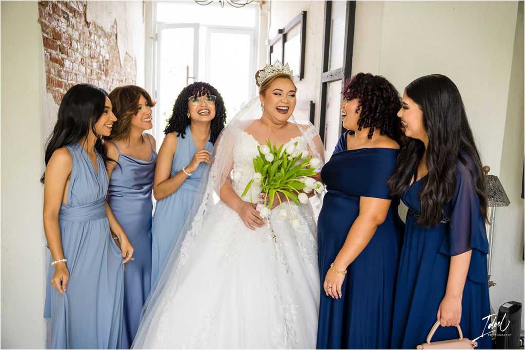 Bridesmaids in blue dresses surround the bride during a candid wedding moment.