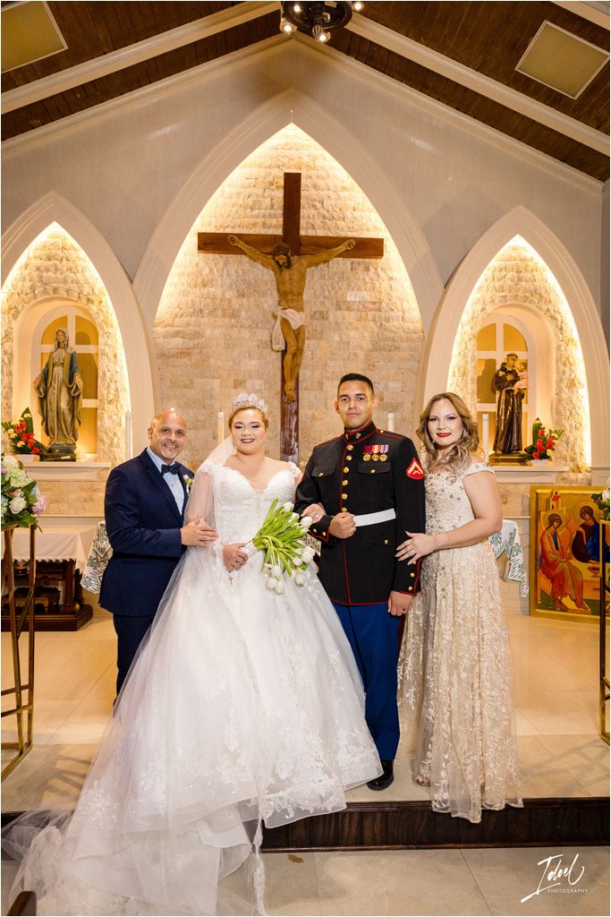 Wedding party posing in front of illuminated church altar with gothic arches and religious iconography.