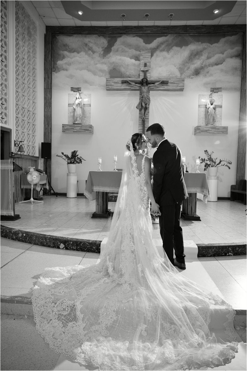Black and white photo of bride and groom sharing a kiss at the altar of a Catholic church on their wedding day.