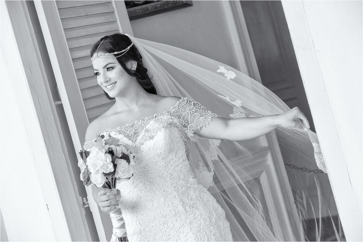 A bride in an elegant white lace wedding dress stands in a doorway holding a bouquet of flowers.