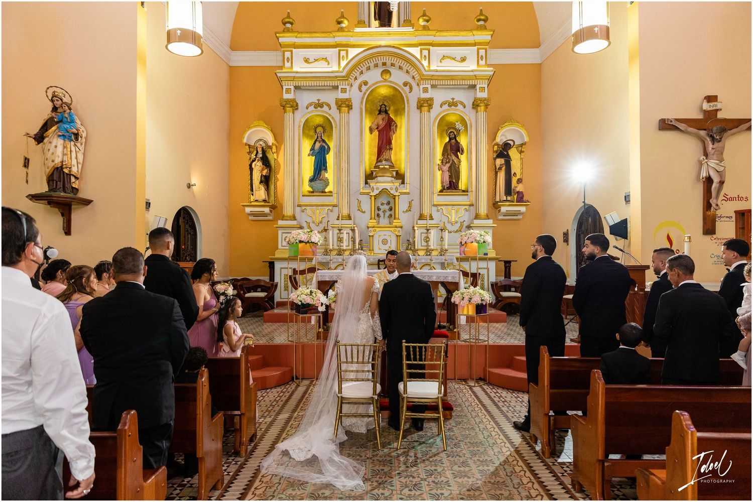 A traditional Catholic church wedding ceremony with ornate gold altar and religious statues in the background.